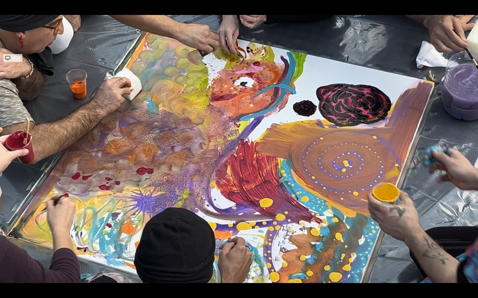 Close detail of hands painting a large shared canvas