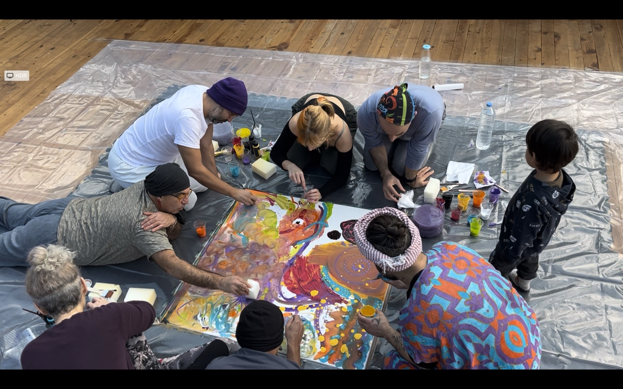 A group collectively painting a large canvas on the floor